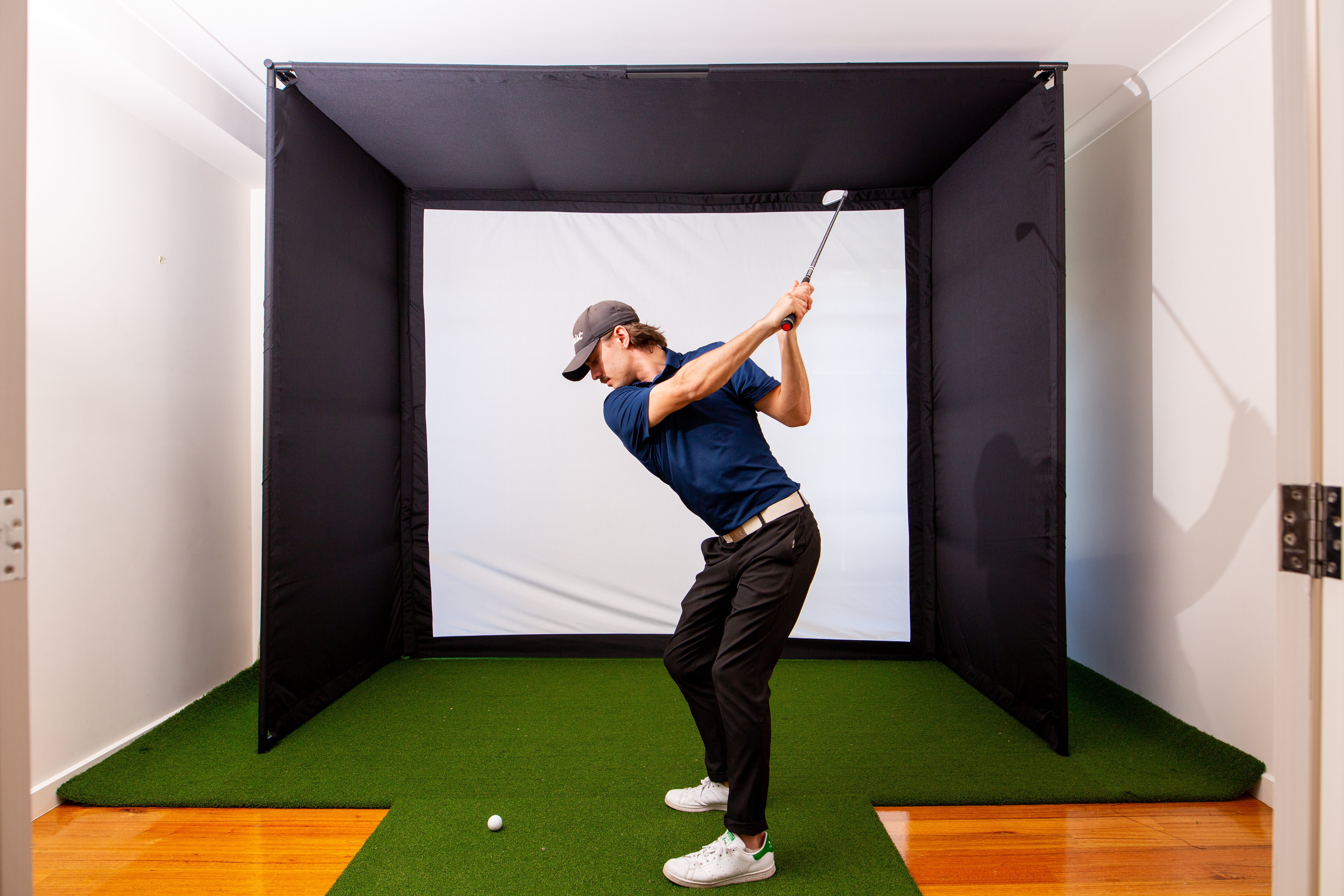 Golfer practicing a full swing in a professional-grade home indoor golf simulator enclosure, demonstrating the immersive training environment for skill improvement and consistent practice.