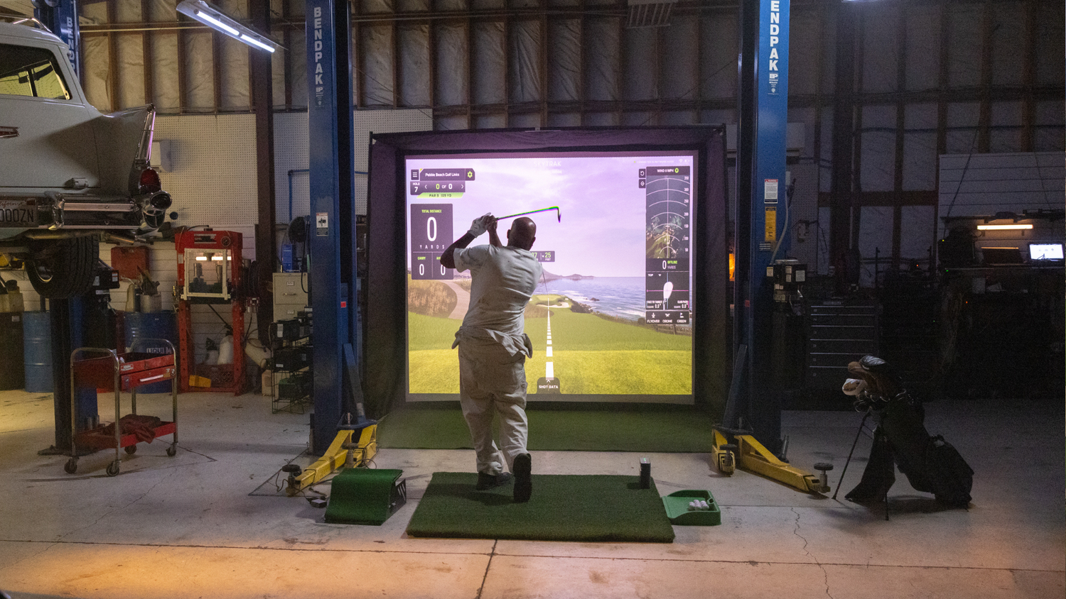 SKYTRAK ST MAX outdoor backyard golf simulator setup at night — home golf simulator with projection screen, fire pit, and patio seating