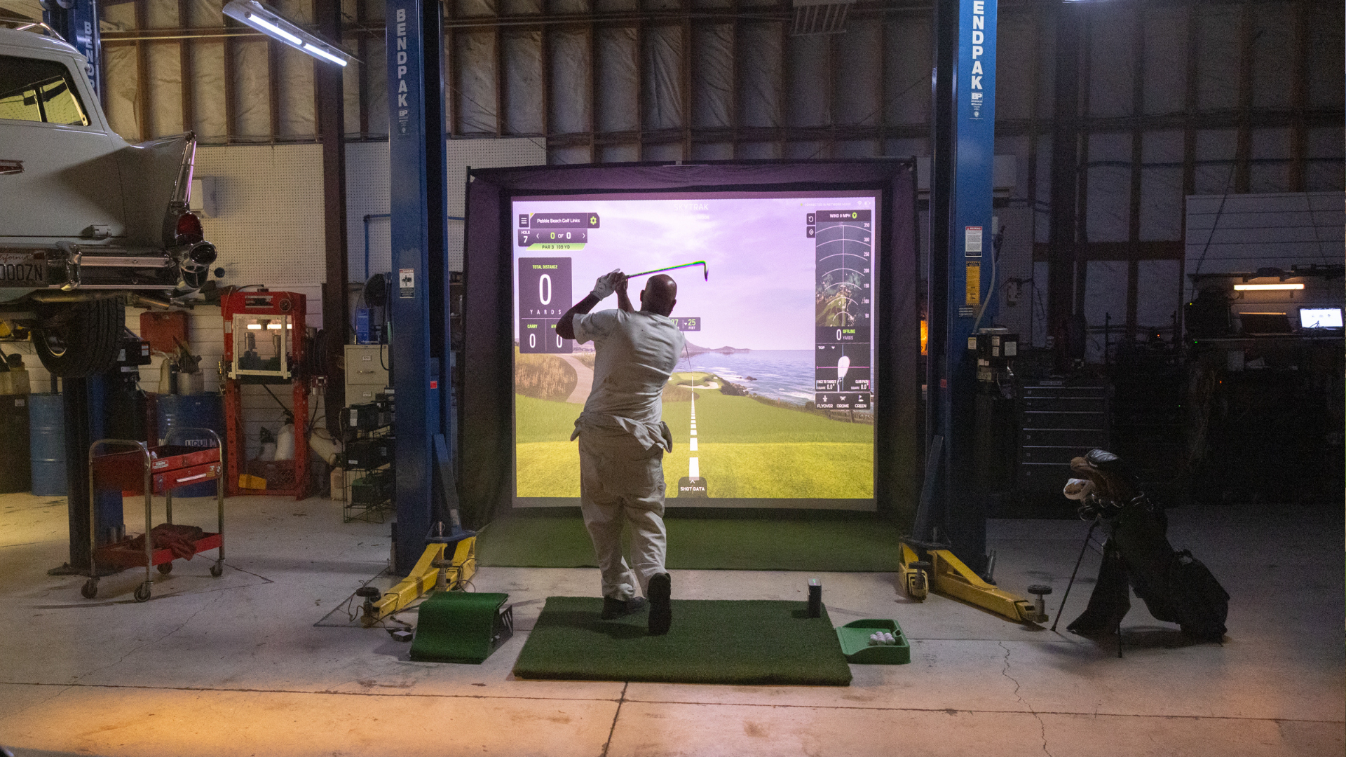 SKYTRAK ST MAX outdoor backyard golf simulator setup at night — home golf simulator with projection screen, fire pit, and patio seating